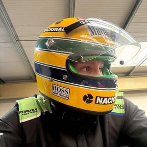 以下が含まれることがあります： 黄色、緑、青のレーシングヘルメット。透明なバイザーが付いており、「NACIONAL」、「BOSS MEN'S FASHION」、「Marlboro」の文字が記されています。ヘルメットは黒と緑のレーシングスーツと共に着用されており、肩には「FRROXX RACE WEAR」の文字が見えます。