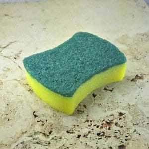 May include: A new, unused, rectangular sponge with a green scrubbing surface and a yellow absorbent base. The sponge has a curved shape and is designed for cleaning.