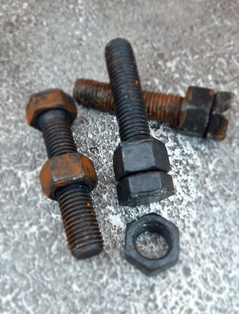 May include: Close-up of several black bolts and nuts with visible rust. The bolts have hexagonal heads and threaded shafts. One nut is separate from the bolts. The objects are on a textured gray surface.