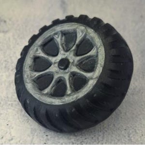 May include: A miniature black tire with a silver rim. The tire has a detailed tread pattern and a multi-spoke wheel design. The wheel is a detailed replica of a car or truck tire.