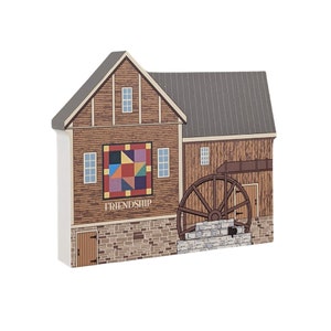 May include: A wooden model of a gristmill with a water wheel. The building is brown with a gray roof and a red, white, and blue quilt hanging on the side. The quilt has the word "Friendship" written below it.