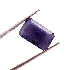 May include: A deep purple gemstone with a rectangular emerald cut. The gemstone is held by a pair of tweezers.