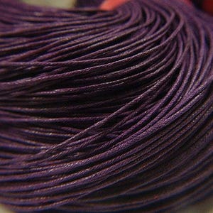 May include: Close-up of a tightly wound ball of dark purple cord. The cord appears to be made of many thin strands, creating a textured surface. The color is a deep, rich shade of purple.