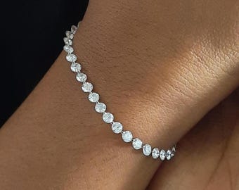 Könnte beinhalten: Ein silberfarbenes Tennisarmband mit einer durchgehenden Reihe runder, klarer, facettierter Steine in einer Metallfassung. Das Armband liegt um das Handgelenk und zeigt die einheitliche Größe und das Funkeln jedes einzelnen Steins.