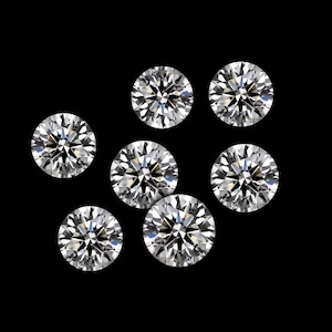 May include: Seven round-cut diamonds are shown against a black backdrop. The diamonds are clear and sparkling, with multiple facets reflecting light. The arrangement is scattered, showcasing the brilliance of the gemstones.