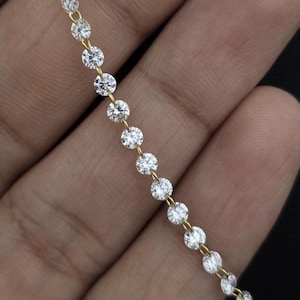 May include: A gold chain necklace featuring a continuous row of round, clear, faceted stones set in individual metal prongs. The stones are arranged in a straight line, creating a sparkling, uniform appearance along the length of the jewellery piece.