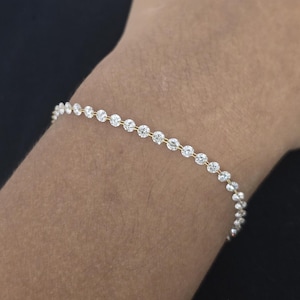 Op de afbeelding: Een delicate gouden armband met een reeks ronde, heldere edelstenen. De armband wordt om een pols gedragen, waardoor de schittering van de stenen wordt benadrukt. Het ontwerp is eenvoudig en elegant, geschikt voor dagelijks gebruik of speciale gelegenheden.