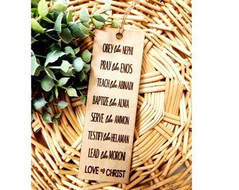 Könnte beinhalten: Ein braunes Holz-Lesezeichen mit dem Text "OBEY like NEPHI, PRAY like ENOS, TEACH like ABINADI, BAPTIZE like ALMA, SERVE like AMMON, TESTIFY like HELAMAN, LEAD like MORON, LOVE as CHRIST" darauf gedruckt.