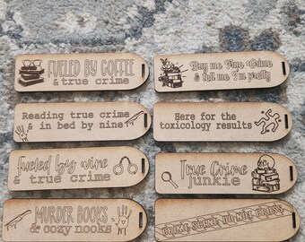 Op de afbeelding: Acht houten borden met gegraveerde tekst en illustraties over true crime en lezen. Zinnen als "Fueled by Coffee & True Crime" en "Murder Books & Cozy Nooks" zijn te zien. De borden zijn waarschijnlijk voor interieurdecoratie.
