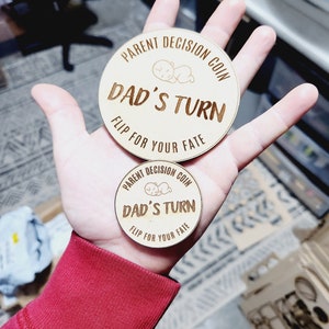 May include: Two wooden coins with the text "PARENT DECISION COIN" and "DAD'S TURN" and the words "FLIP FOR YOUR FATE" on the bottom.