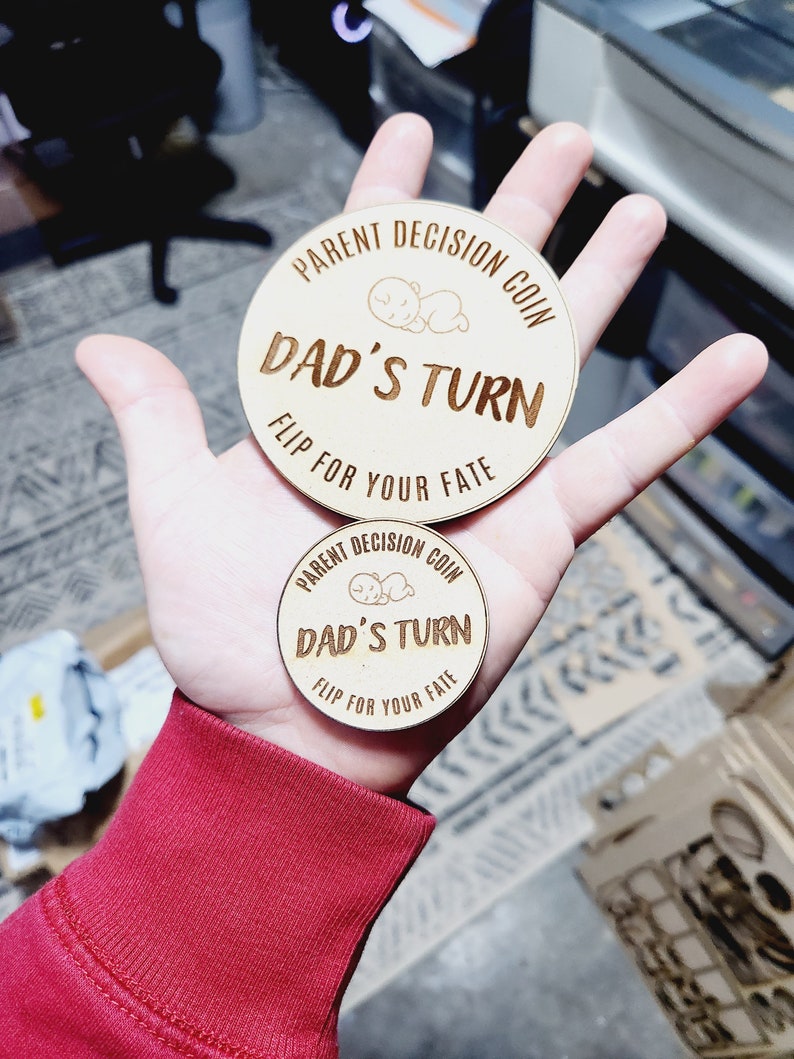 May include: Two wooden coins with the text "PARENT DECISION COIN" and "DAD'S TURN" and the words "FLIP FOR YOUR FATE" on the bottom.