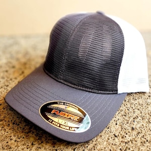 Könnte beinhalten: Eine graue und weiße Mesh-Baseballkappe mit einem Flexfit-Etikett. Das Etikett lautet "The Original Flexfit L/XL It Fits Your Life."