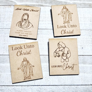May include: Four wooden plaques with the phrase "Look Unto Christ" and different images of Jesus Christ. The plaques are all the same size and shape, and they are all made of light brown wood.