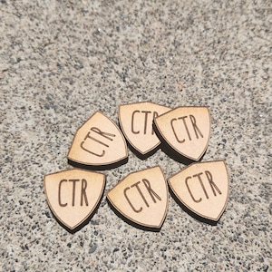 May include: Six wooden guitar picks with the letters "CTR" engraved on each pick. The picks are arranged in a circle on a gray concrete surface.