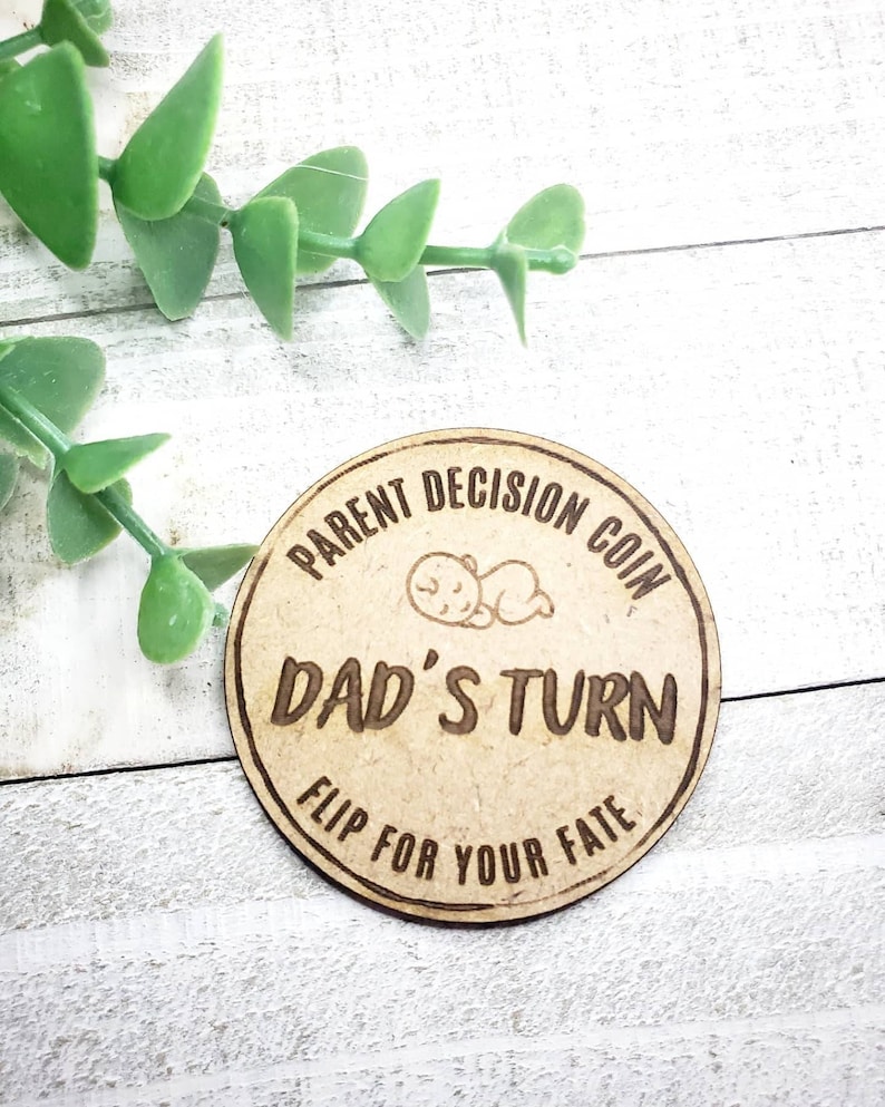 May include: A wooden coin with the text "Parent Decision Coin" and "Dad's Turn" with a sleeping baby graphic. The coin also has the text "Flip for your fate".
