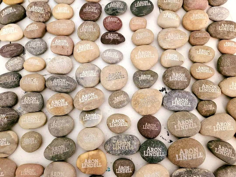 May include: A collection of smooth, gray and brown stones with the name "Aron Lindell" engraved on each one.