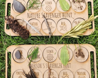 May include: Two wooden nature scavenger hunt boards with various items like a rock, pinecone, feather, and stick. Each board has labeled circles with the text "NATURE SCAVENGER HUNT" and "EMERSON'S SCAVENGER HUNT". The boards are on green grass.