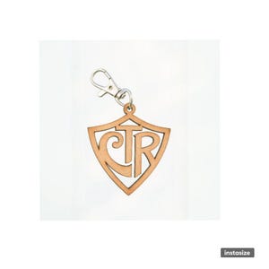 May include: A wooden keychain with a shield shape and the letters "CTR" cut out. The keychain is light brown and has a silver-colored clasp. The design is simple and elegant, suitable for everyday use.