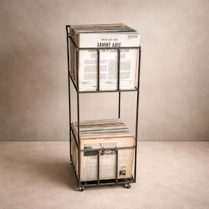 May include: A black metal record storage rack on wheels, holding numerous vinyl records. The top shelf displays a record with the text "Swing and Sway Sammy Kaye Dancing on a Silk Cloud". The rack has two shelves and a rectangular design.