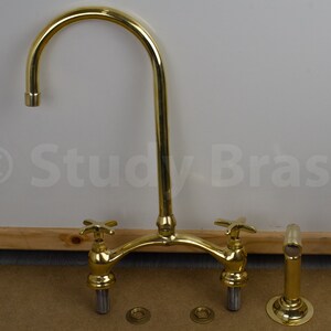 以下が含まれることがあります： 高アーチの注ぎ口と2つのハンドルが付いた金メッキのキッチン蛇口。蛇口はカウンタートップに取り付けられており、磨かれた仕上げになっています。
