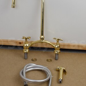 以下が含まれることがあります： 2つのハンドルと引き出し式のスプレイヤーが付いたゴールド調のキッチン蛇口。蛇口はホースとベースプレートで組み立てられています。