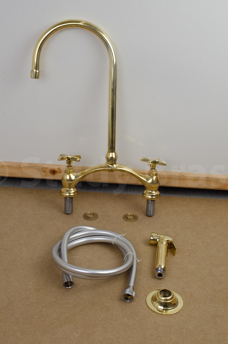 以下が含まれることがあります： 2つのハンドルと引き出し式のスプレイヤーが付いたゴールド調のキッチン蛇口。蛇口はホースとベースプレートで組み立てられています。
