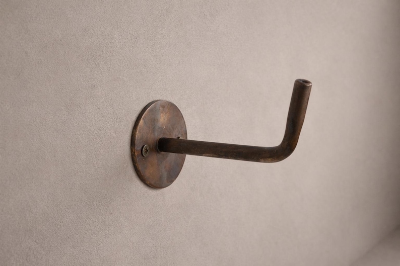 Peut inclure: Un crochet mural de couleur bronze avec une base circulaire et un bras incurv&eacute;. Le crochet est mont&eacute; sur un mur gris clair. Le crochet est en m&eacute;tal et a un aspect vintage ou antique.