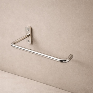 May include: A polished chrome towel holder mounted on a neutral-toned wall. The holder features a rectangular mounting plate with two screws and a curved bar for hanging towels. The design is simple and modern.