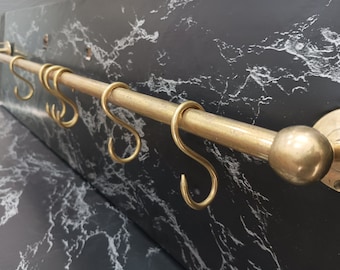 May include: A brass kitchen utensil rack with a black marble background. The rack has a round knob on one end and five S-shaped hooks.