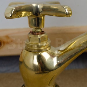 以下が含まれることがあります： 十字形のハンドルが付いた金色の真鍮製の蛇口。蛇口は丸いベースと、外側に曲がって下向きになっている注ぎ口を持っています。