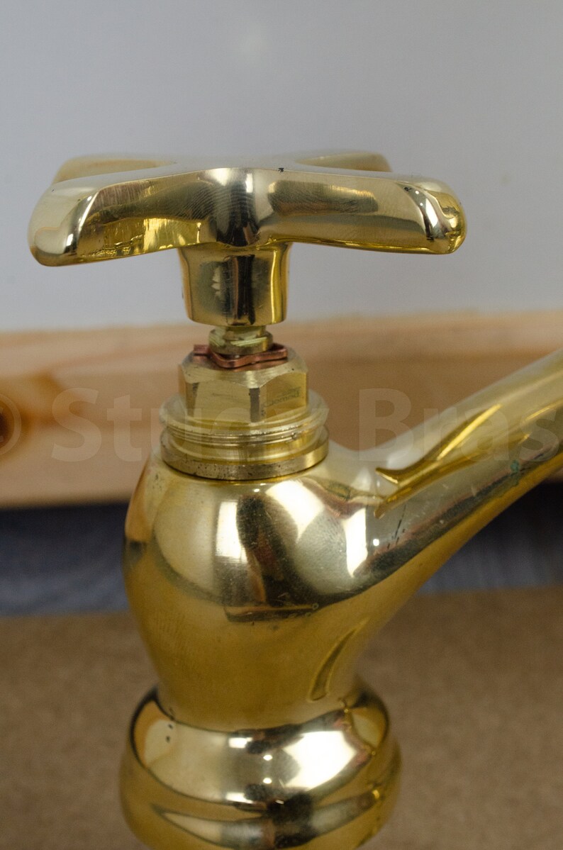 以下が含まれることがあります： 十字形のハンドルが付いた金色の真鍮製の蛇口。蛇口は丸いベースと、外側に曲がって下向きになっている注ぎ口を持っています。