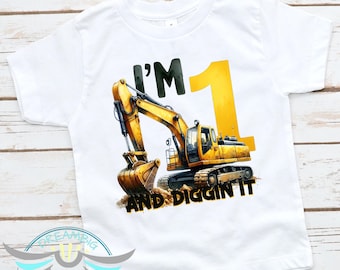 May include: White short-sleeved t-shirt with a yellow excavator graphic and the text "I'm 1 and Diggin' It".