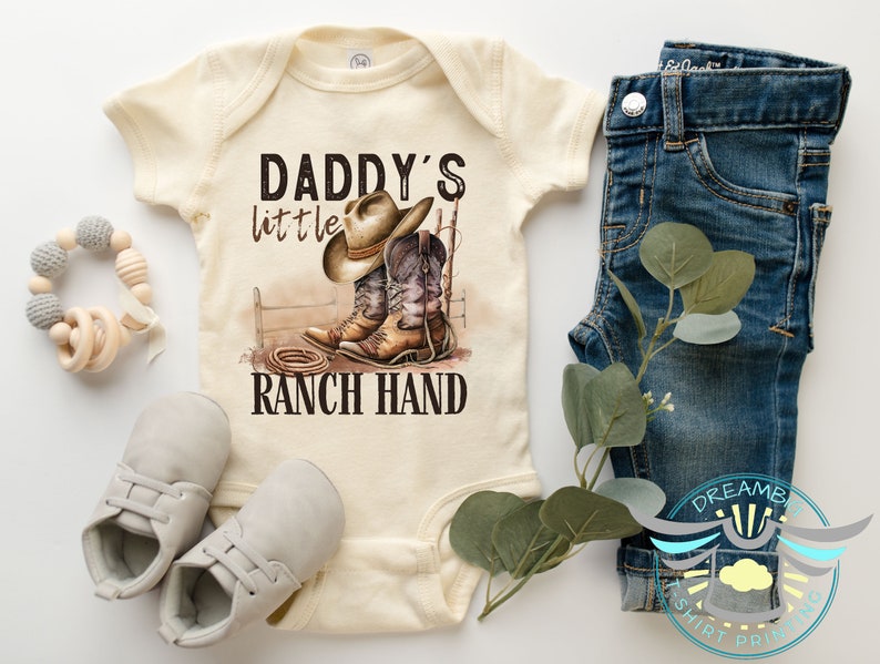 Daddy's little ranch hand baby bodysuit. Perfect for your little wrangler. This cute and comfy outfit is ideal for your tiny cowboy. Great for photos, special occasions or everyday wear. A must have for country loving family. Natural color bodysuit.