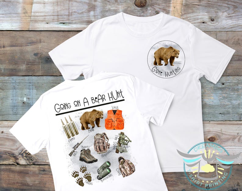 Puede incluir: Camiseta blanca con un gr&aacute;fico de un oso marr&oacute;n y el texto "Going on a Bear Hunt". La parte posterior de la camiseta presenta un oso, un chaleco, binoculares, un rifle, botas, municiones y un abrigo.