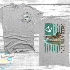 May include: Gray t-shirt with a green-winged teal duck on a distressed American flag design on the back. The front of the shirt has a small circle logo with the text "Duck Hunter Authentic Outdoors".
