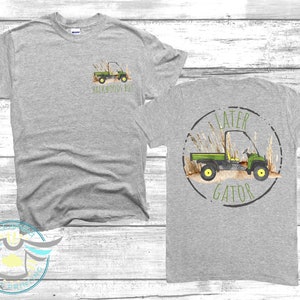 May include: Grey t-shirt with a green utility vehicle graphic and the text "Backwoods Boy" on the front. The back of the shirt has a green utility vehicle graphic inside a circle with the text "Later Gator".