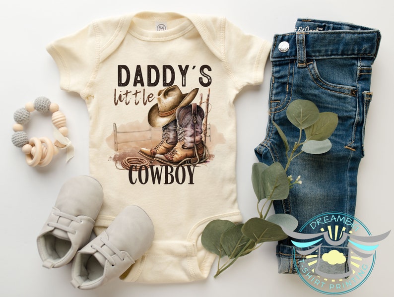 Daddys little cowboy baby bodysuit. Perfect for your little wrangler. This cute and comfy outfit is ideal for your tiny cowboy. Great for photos, special occasions or everyday wear. A must have for country loving family. Natural color bodysuit.