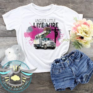 May include: White t-shirt with a pink watercolor background and a white truck with a bucket truck. The text "Uncle's Little Live Wire" is printed on the shirt.