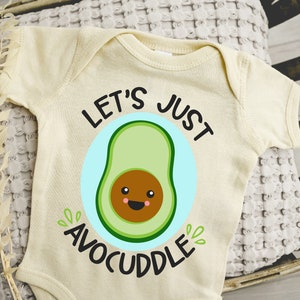 May include: A cream-colored baby onesie with a green avocado graphic and the text "Let's Just AvoCuddle".