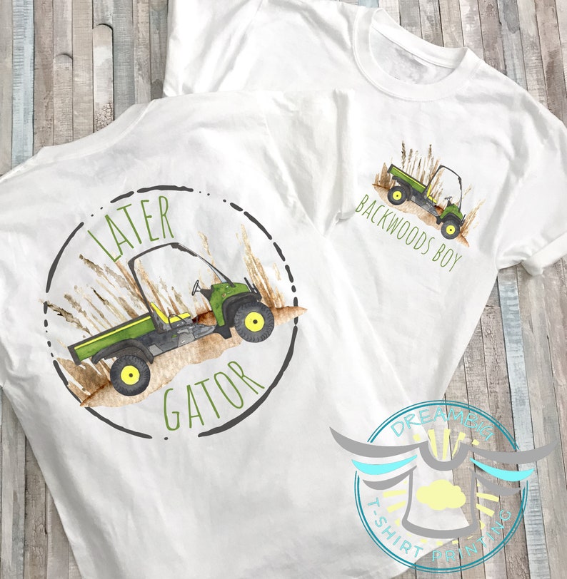 May include: Two white t-shirts featuring a green and black utility vehicle design. One shirt reads "Later Gator" with a circle around the vehicle. The other shirt reads "Backwoods Boy" with the vehicle in the centre.