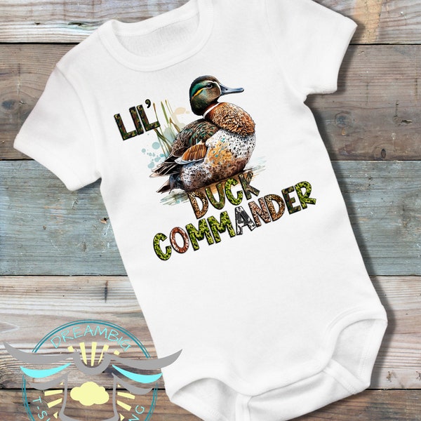 May include: White baby bodysuit with a green, brown and white duck illustration. The text "Lil' Duck Commander" is printed on the bodysuit.