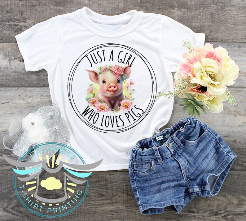 May include: White t-shirt with a pink pig wearing a flower crown in a circle with the text "Just a girl who loves pigs".