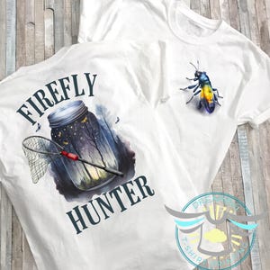 May include: White t-shirt with a blue and black illustration of a jar filled with fireflies and a net. The text "FIREFLY HUNTER" is printed on the shirt.