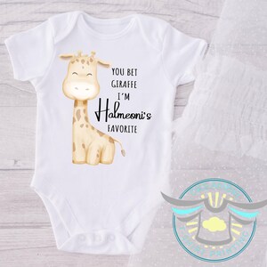 May include: White baby bodysuit with a giraffe illustration and the text "YOU BET GIRAFFE I'M Halmeoni's FAVORITE". The giraffe is tan with brown spots. The bodysuit has short sleeves.
