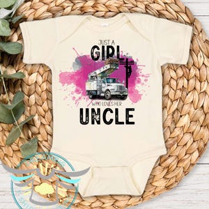 May include: Cream-colored baby bodysuit with the text "Just a Girl Who Loves Her Uncle." The design features a utility truck with a cherry picker, set against a pink watercolor splash and a power line.