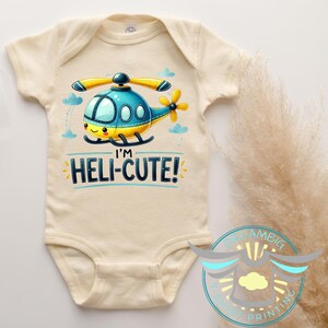 May include: A cream colored baby onesie with a cartoon helicopter graphic and the text "I'm Heli-Cute!" printed on the front.