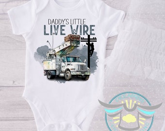 May include: White baby bodysuit with a blue and gray graphic of a utility truck and a lineman working on a power line. The text "Daddy's Little Live Wire" is printed on the shirt.