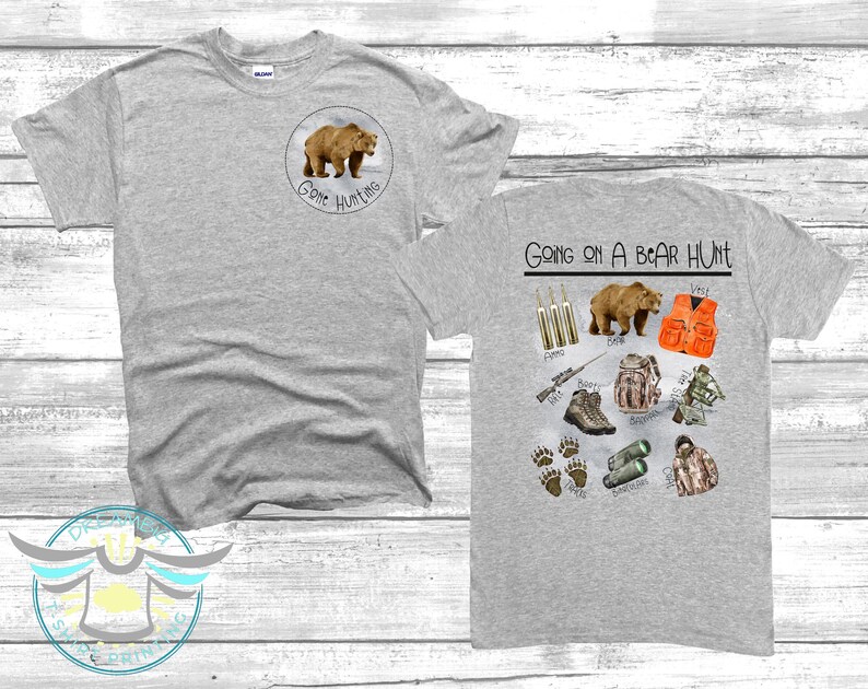 Puede incluir: Dos camisetas grises con tem&aacute;tica de caza de osos. La parte delantera de una camiseta tiene un oso marr&oacute;n con el texto "Gone Hunting". La parte trasera de la otra camiseta tiene el texto "Going on a Bear Hunt" e ilustraciones de equipo de caza, incluyendo un oso, un rifle, botas y un chaleco de caza.