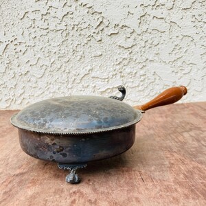 May include: Silver serving dish with a wooden handle and three feet. The dish has a lid and is tarnished.