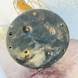 Pu&ograve; includere: Il lato inferiore di una base di ventilatore vintage in metallo. La base &egrave; nera e ha diversi fori per viti.